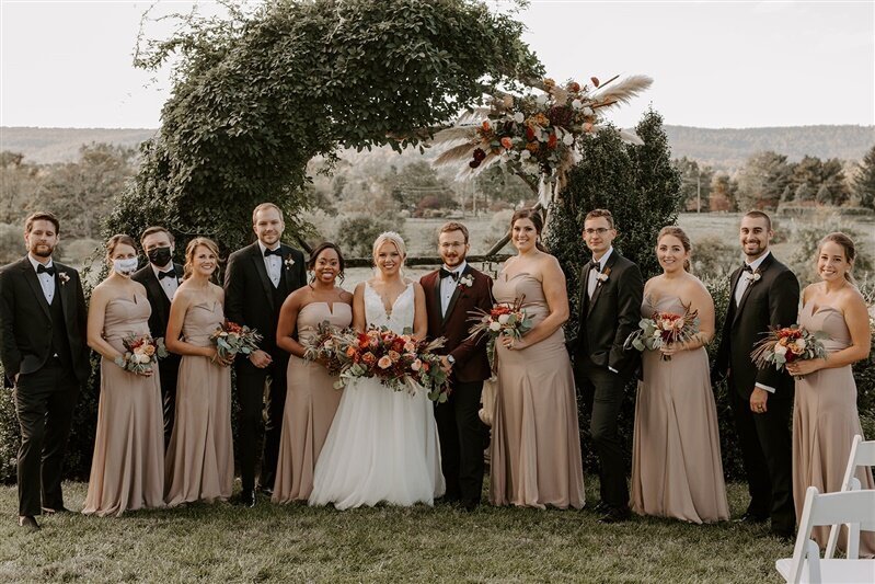 Entire wedding party with bouquets in front of the decorated wedding arch