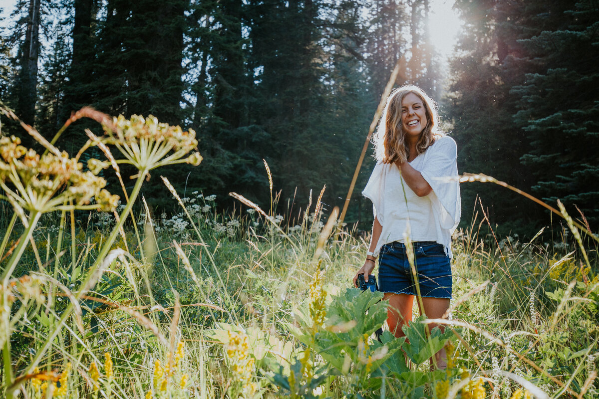 Girl stands in meadow smiling with the sun at her back