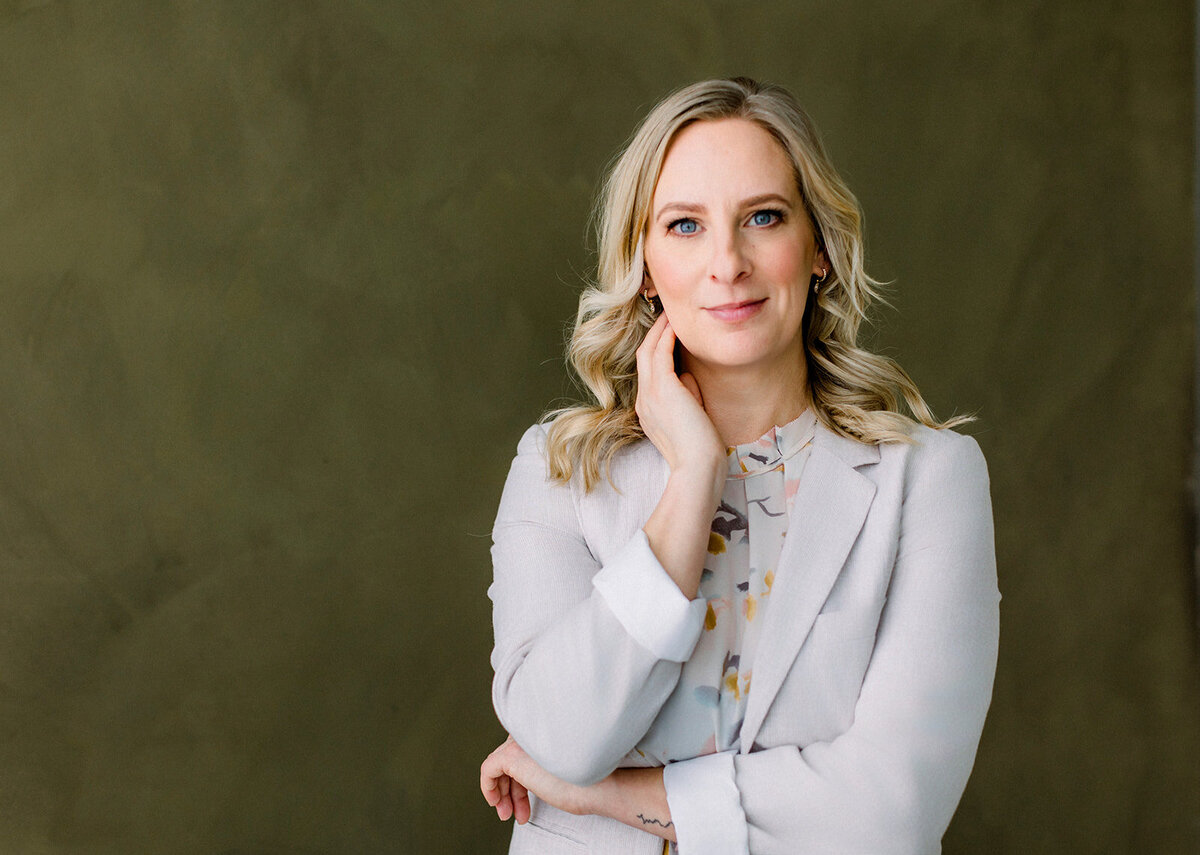 Brand headshot of a blonde Calgary business woman with her hand on her neck against a dark green background.