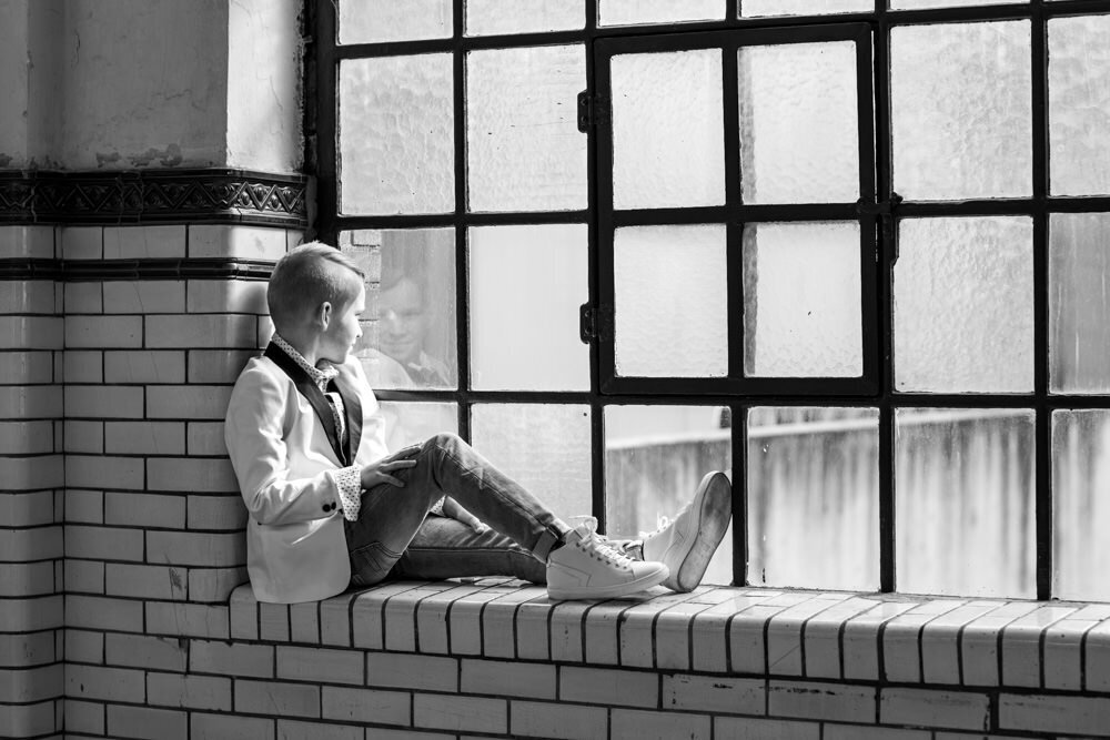 stoere communiefoto jongen in vensterbank bij raam