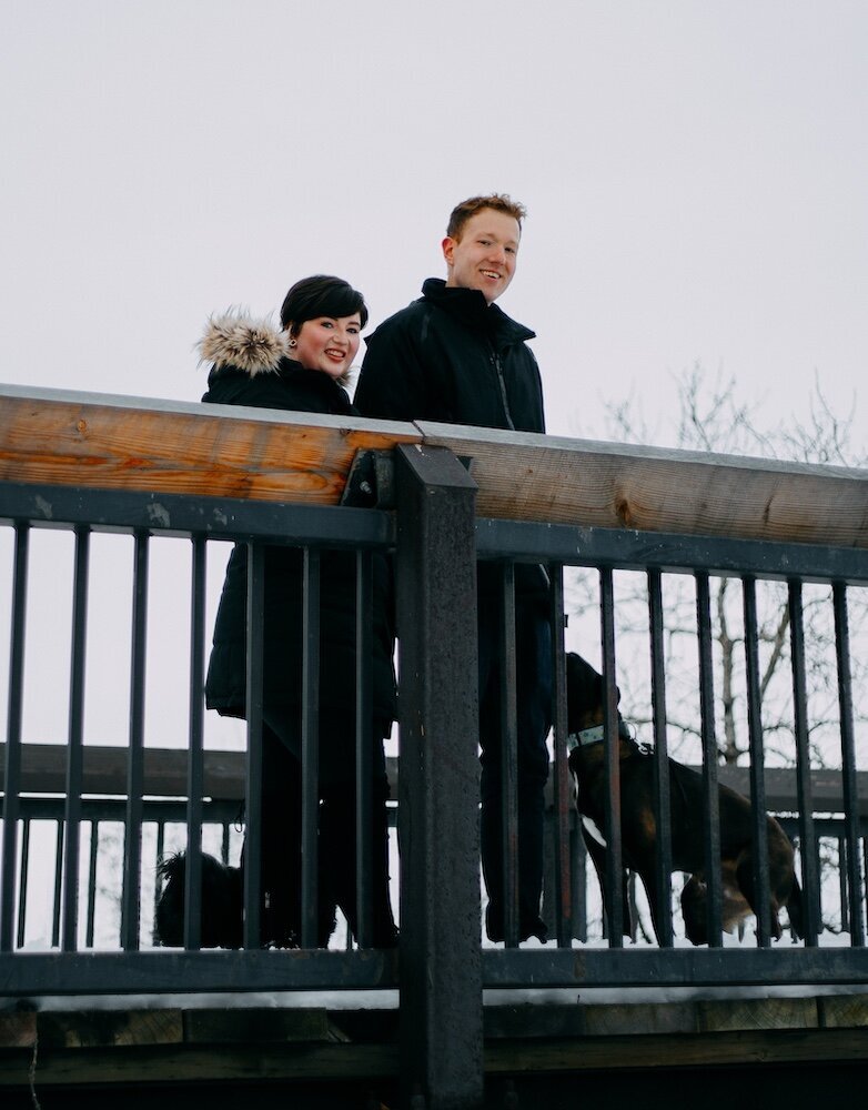 A couple look out over a bridge with their two dogs