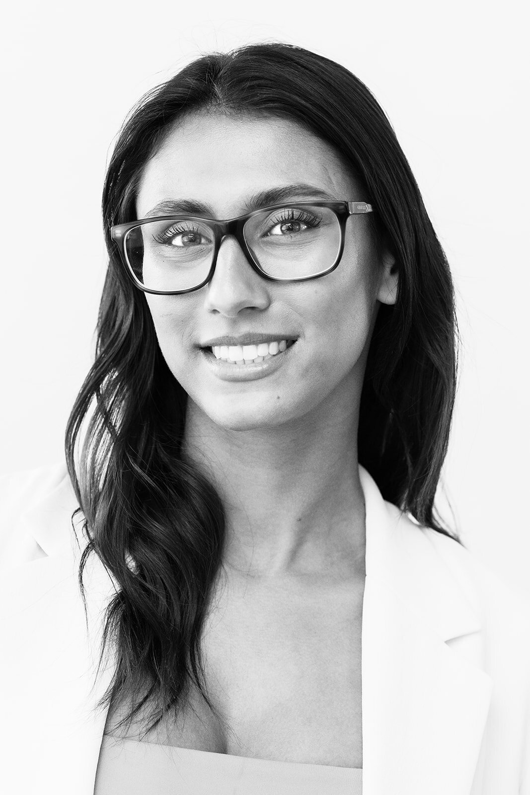 Black and white close-up image of a beautiful woman smiling and wearing glasses and a light shirt.