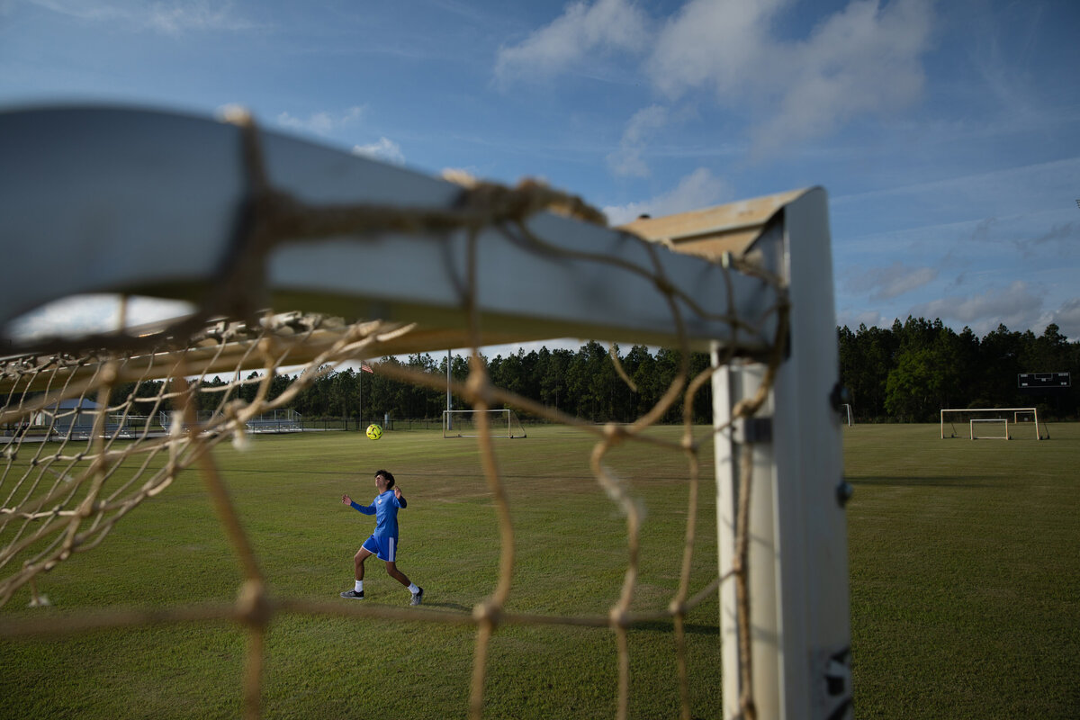A boy playing soccer seen through the goal net