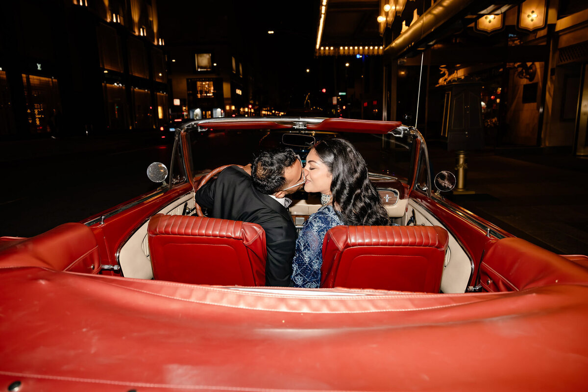 Indian bride and groom kiss in a red Mustang outside the Drake Hotel