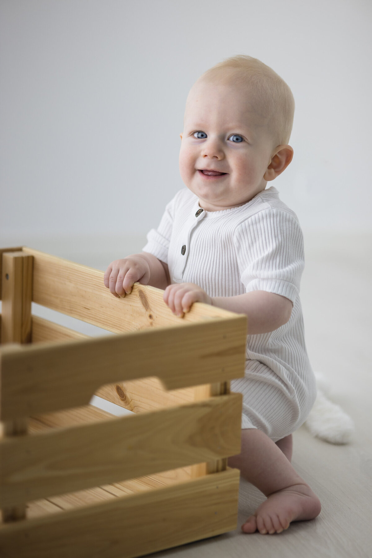 En ettåring holder en trefarget kasse og ser mot kamera. Iført en hvit body. Fotografert i Studio Landmark, Fyllingsdalen.