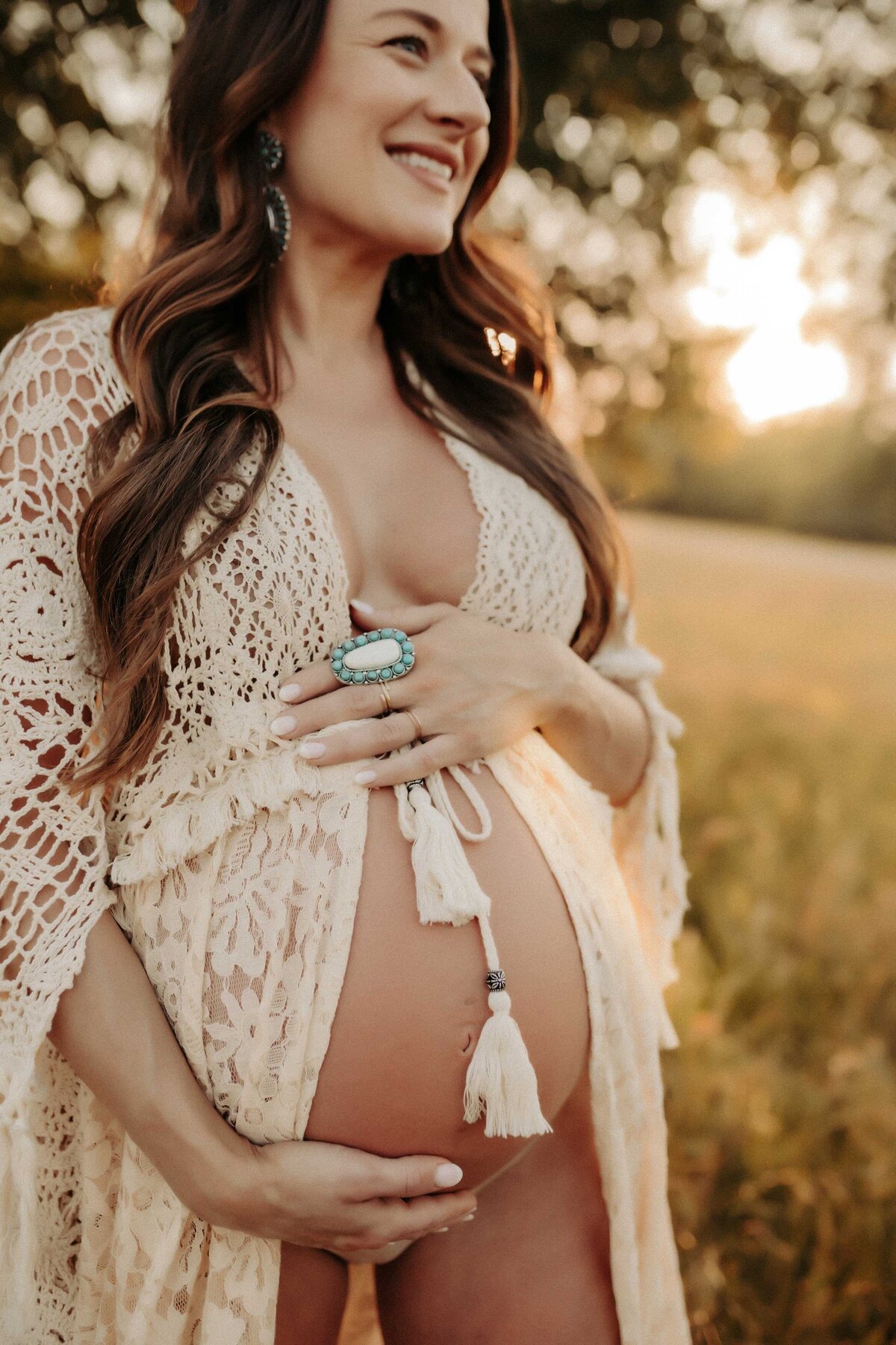 Pregnant woman wearing a macrame robe and holding her belly and smiling