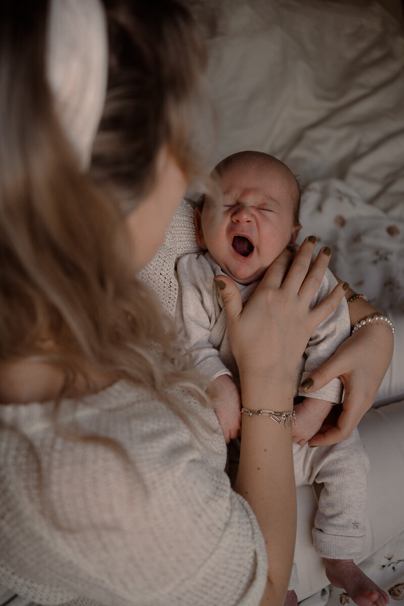 Moeder heeft pasgeboren baby vast terwijl de baby een grote gaap laat zien tijdens een newbornshoot