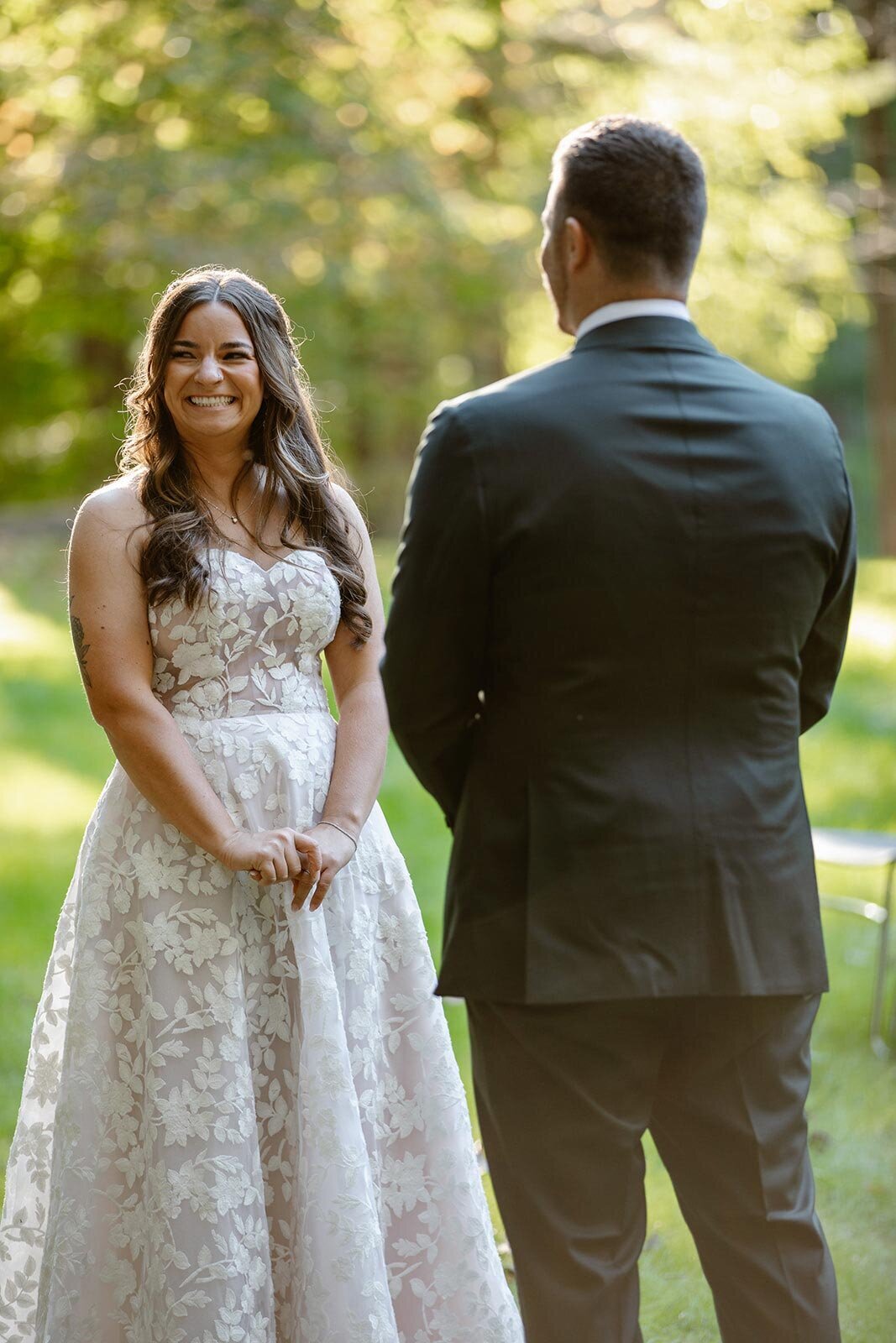 A bride and groom standing listening to their wedding officiant during their wedding ceremony. The bride has a big smile on her face.