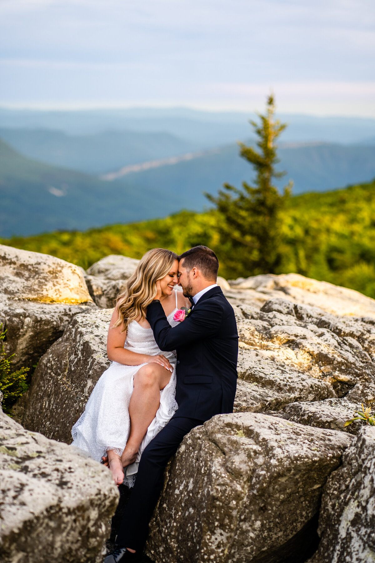 Bride and groom cuddling on rocks with mountain view behind them