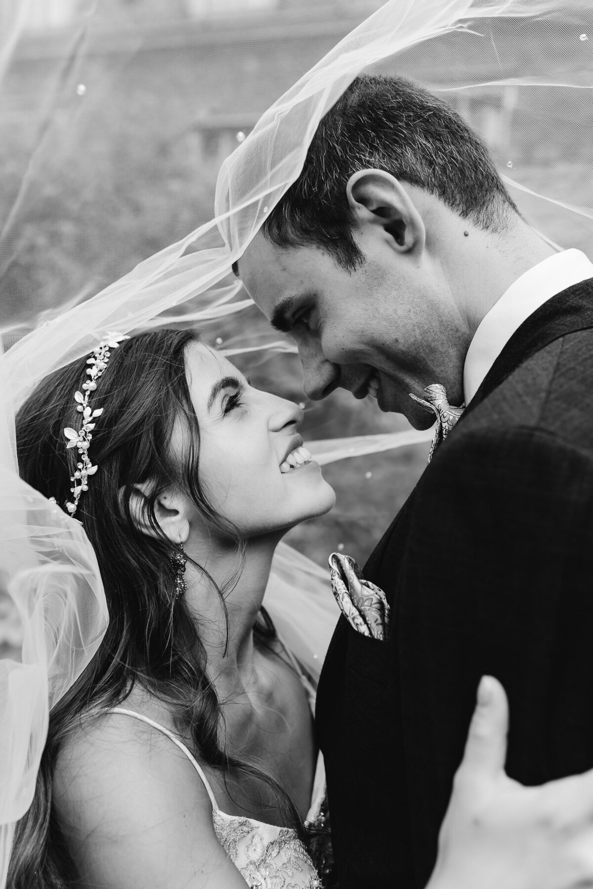 smiling bride and groom underneath vail touching noses