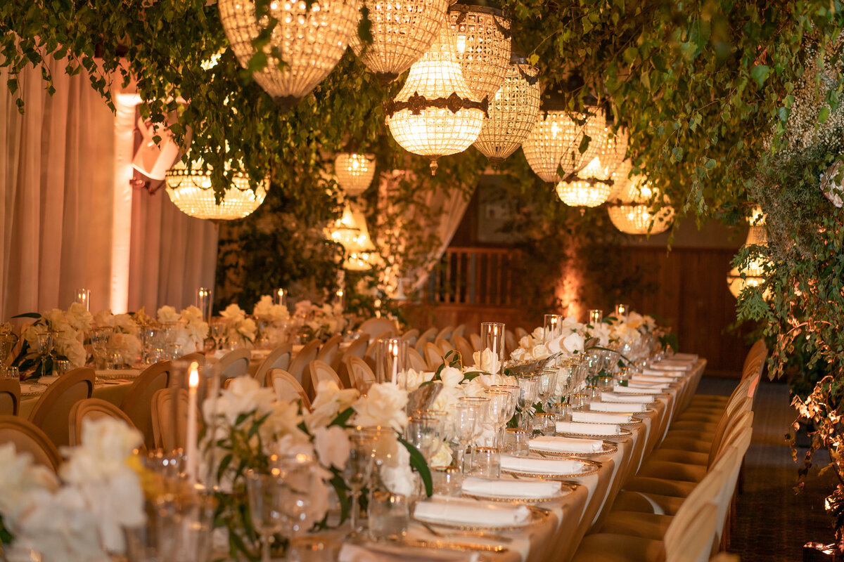 A rustic wedding aisle lined with baskets of greenery frames a bride in a white dress holding her bouquet.