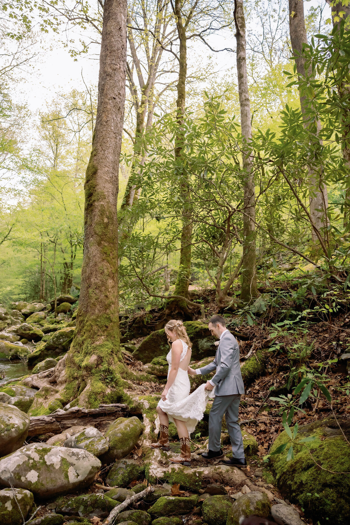 Eloping to Gatlinburg with candid wedidn gpictures of groom carrying his brides train as she hikes up river rocks