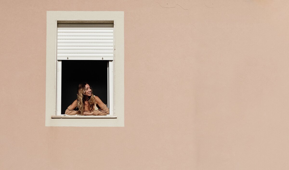 Smiling woman gazes out the window of her Casa Rosa, capturing a serene and joyful moment.