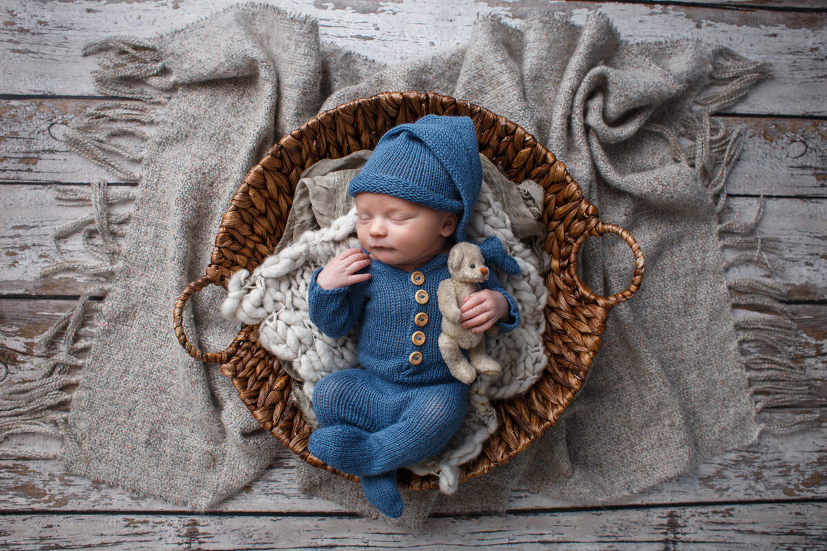 Portrait of an infant wearing a blue sleeper and wearing a matching sleep cap holding a teddy bear