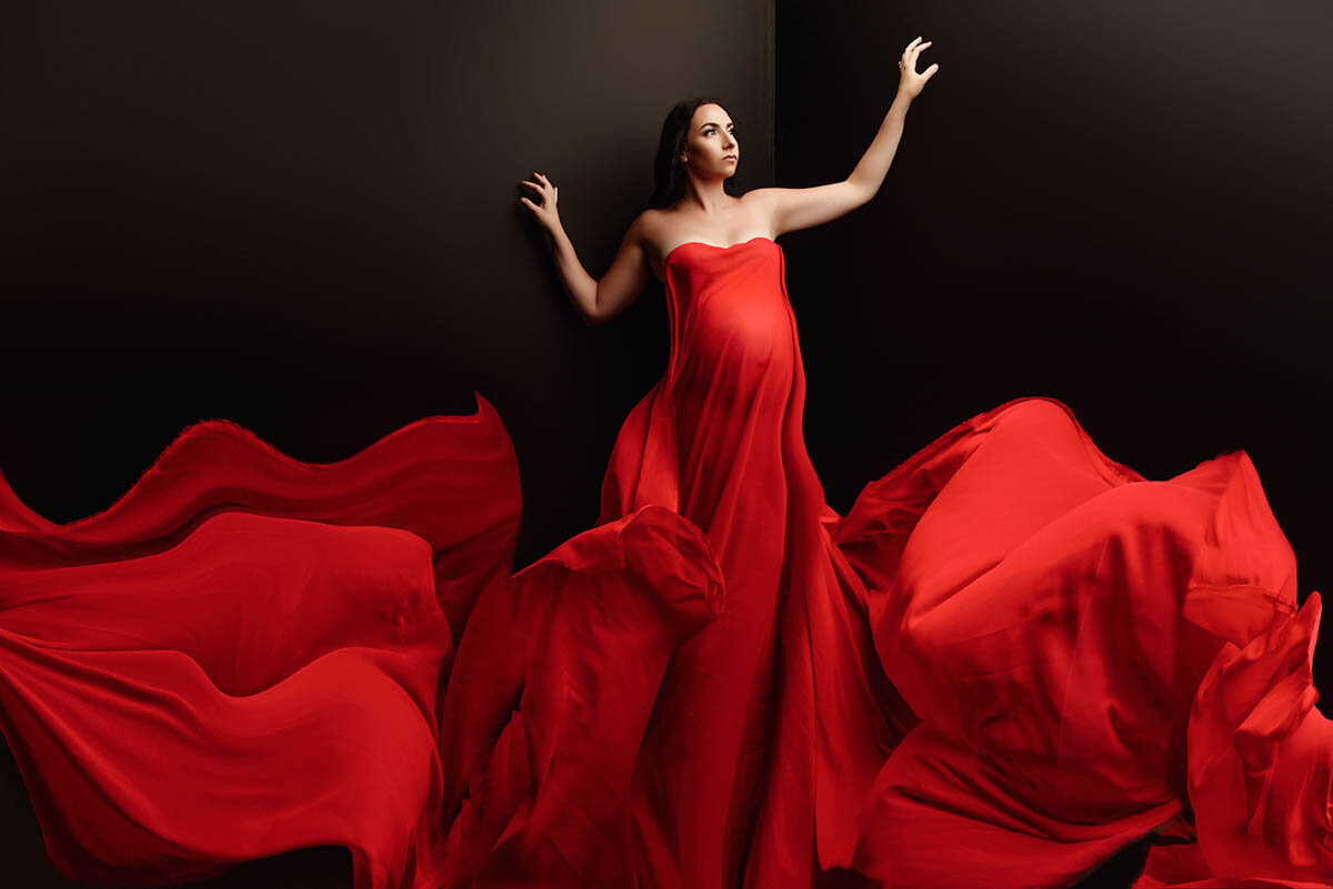 Stunning portrait of woman in red flowing dress for maternity shoot