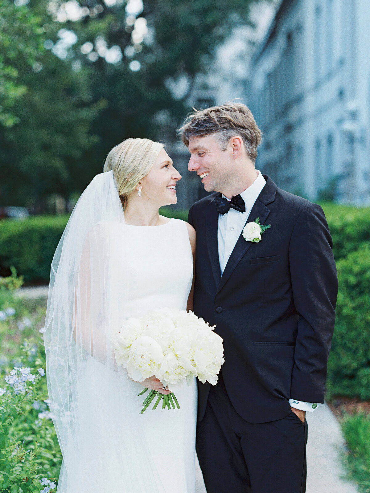 Bride and groom smile at each other on a Charleston sidewalk