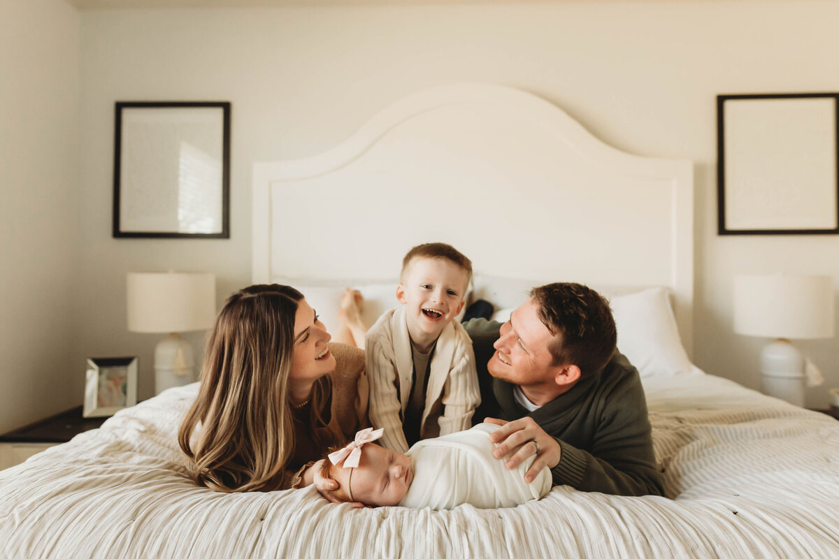 Family snuggling with newborn baby on white bed