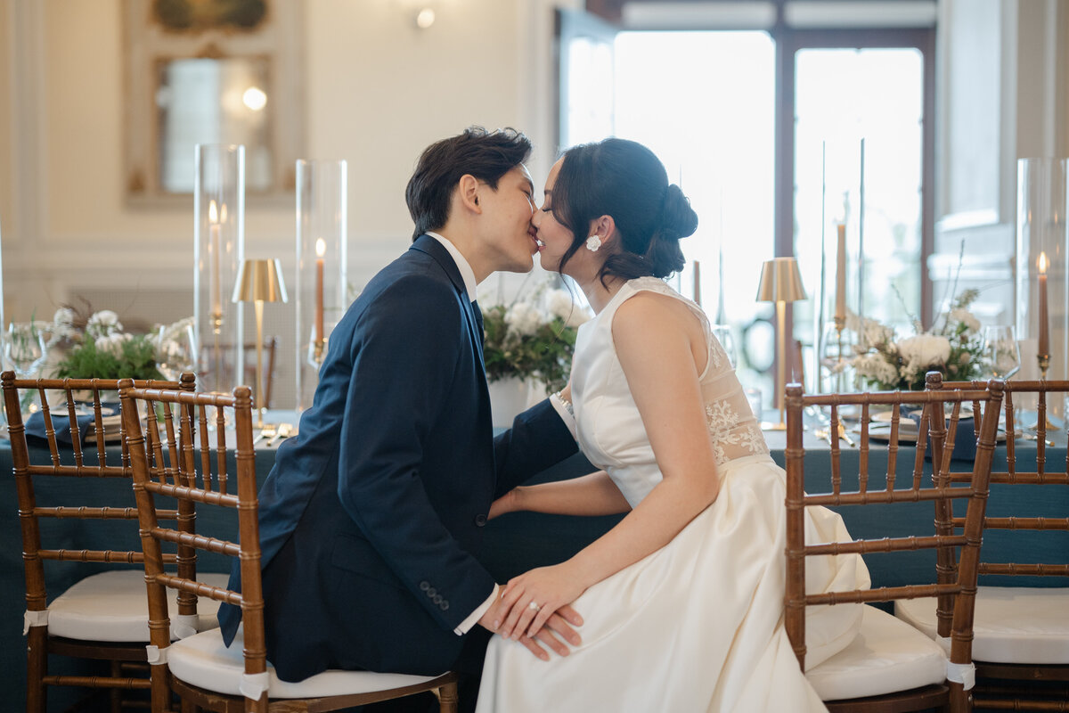 Les mariés s’étirent doucement l’un vers l’autre pour s’embrasser pendant la réception, moment tendre et spontané saisi dans l’atmosphère conviviale d’un mariage romantique célébré au Québec.