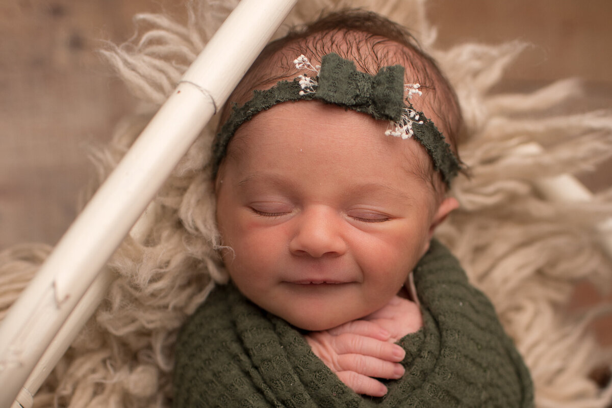 Baby girl wrapped up in green wrap with matching headband, smiling at the camera