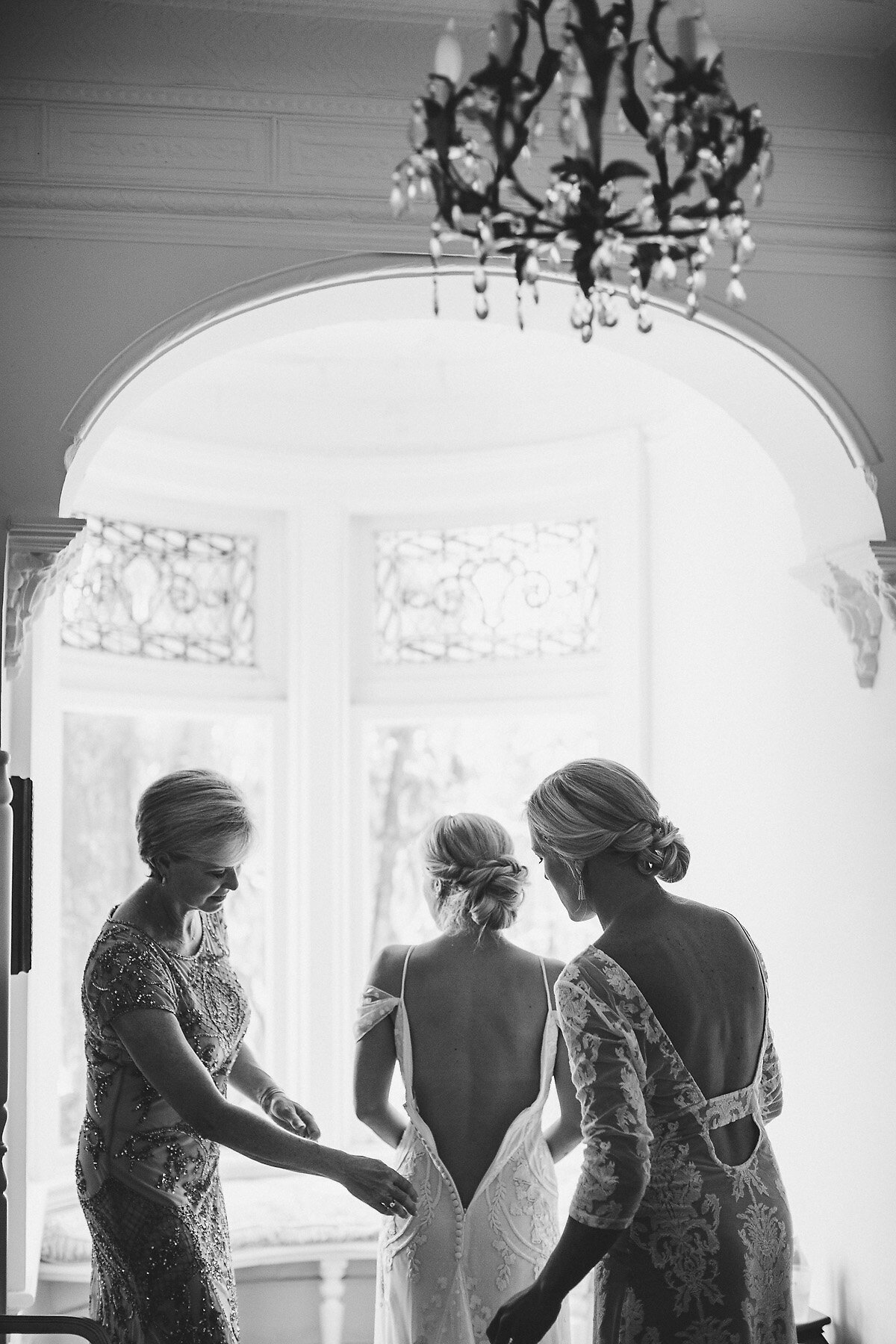 Mother helping bride put on wedding dress.