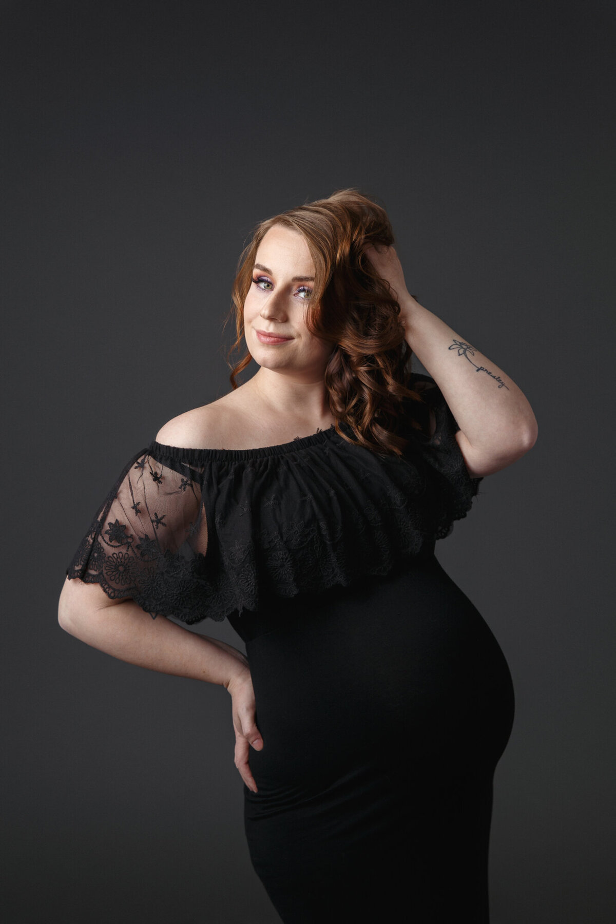 Close up portrait of a pregnant mother to be wearing a black dress with lace slesses against a dark gray background