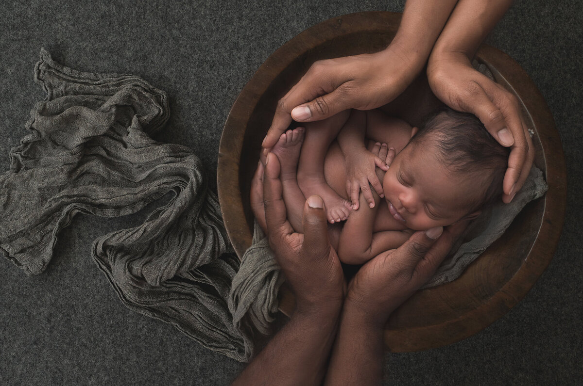 a baby boy in a dark wood basket with gray backdrop and blankets