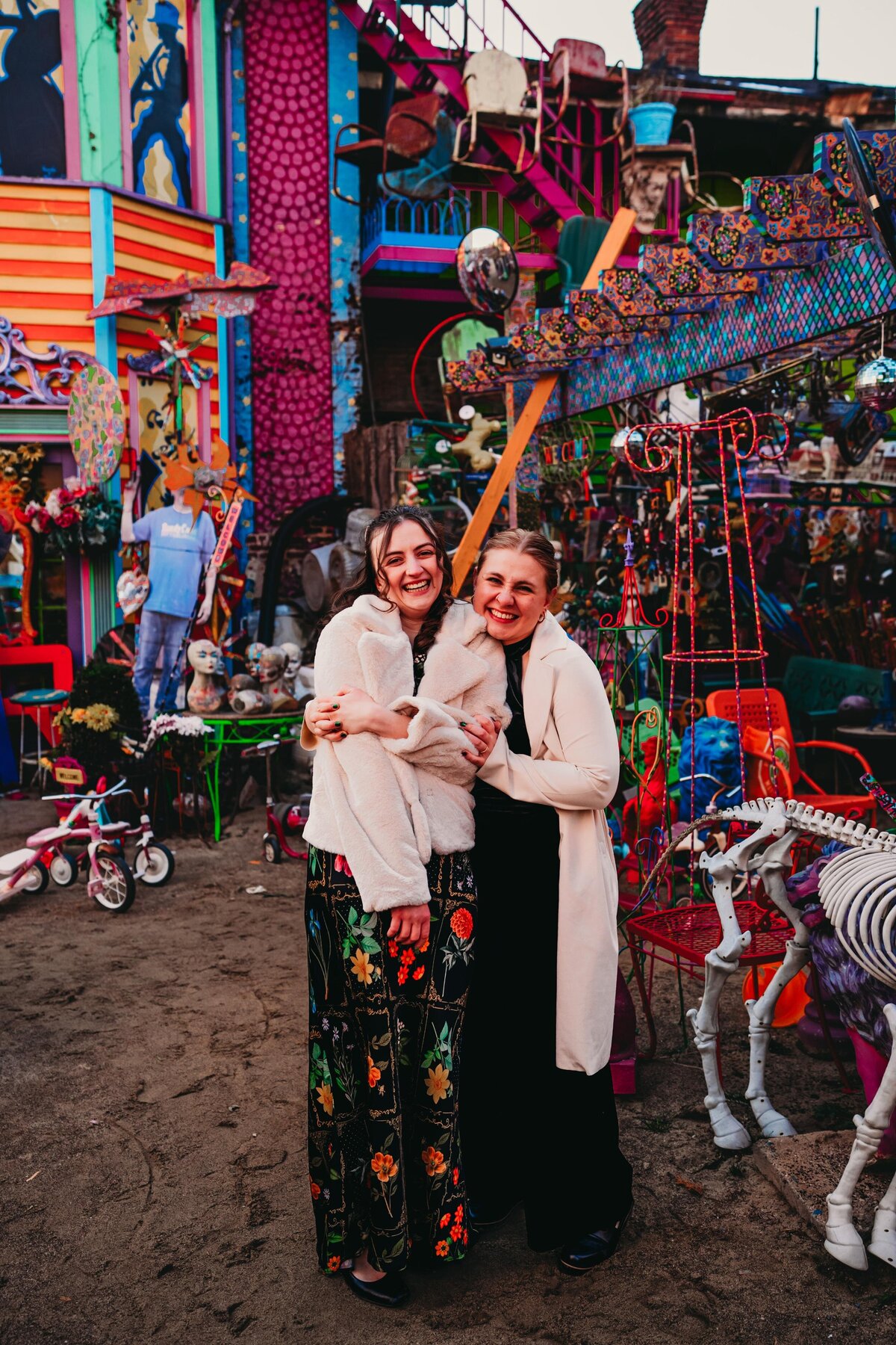 Queer couple embraces in front of the colorful mural at Randyland in Pittsburgh, celebrating their love with a joyful wedding portrait.