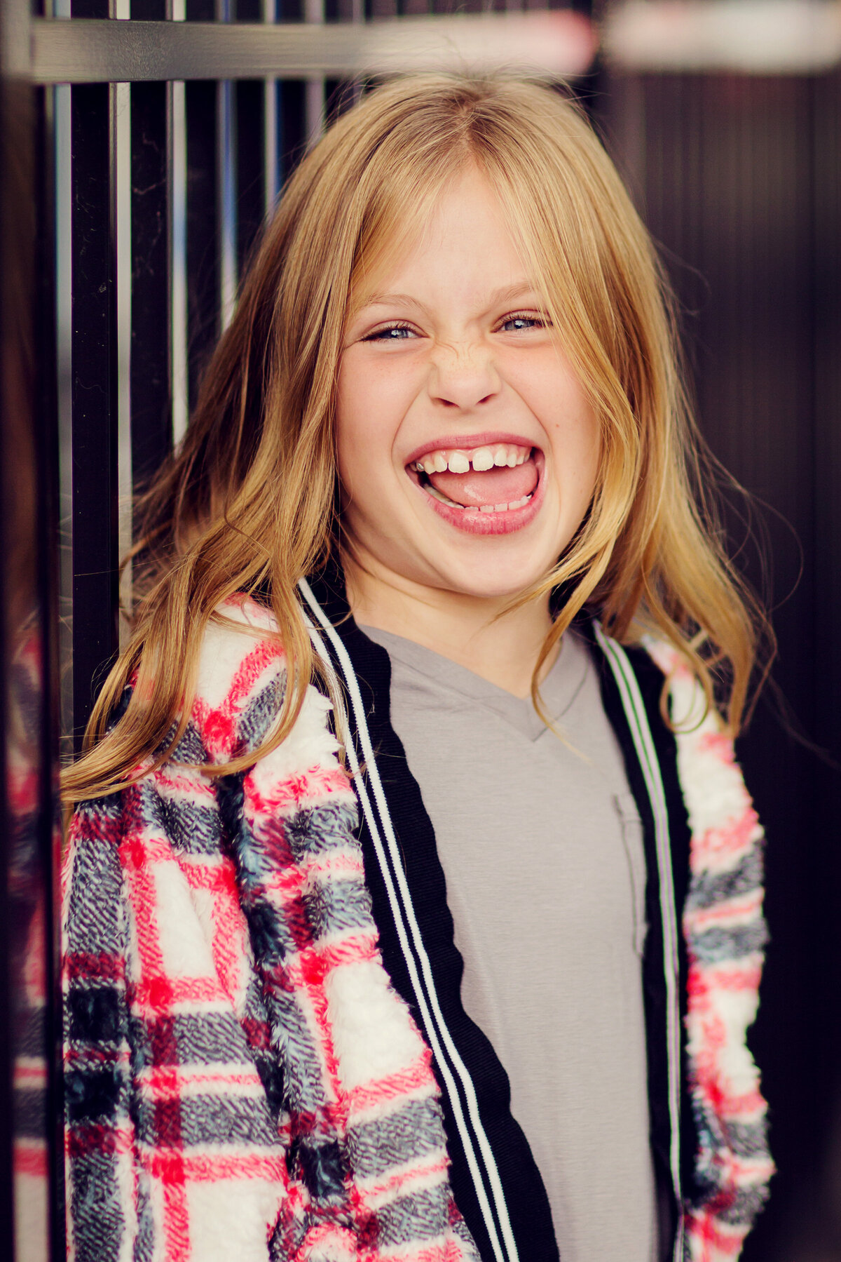 Cute girl laughing hard with a big, crooked smile. She's wearing a plaid jacket that is red, white and black.