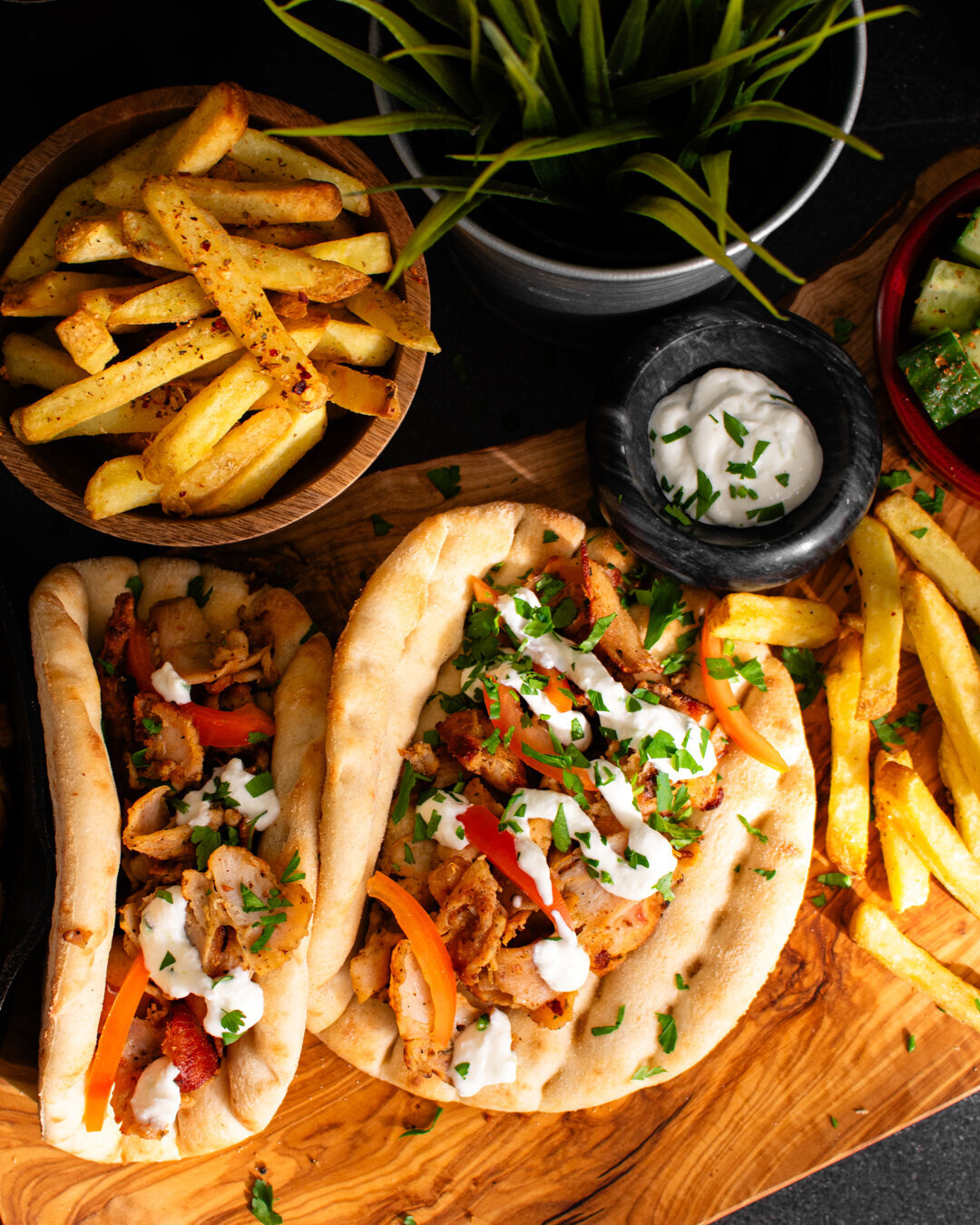 Chicken Gyros Meal with skin on fries on an olive wood board with tzatziki dressing and tomato.