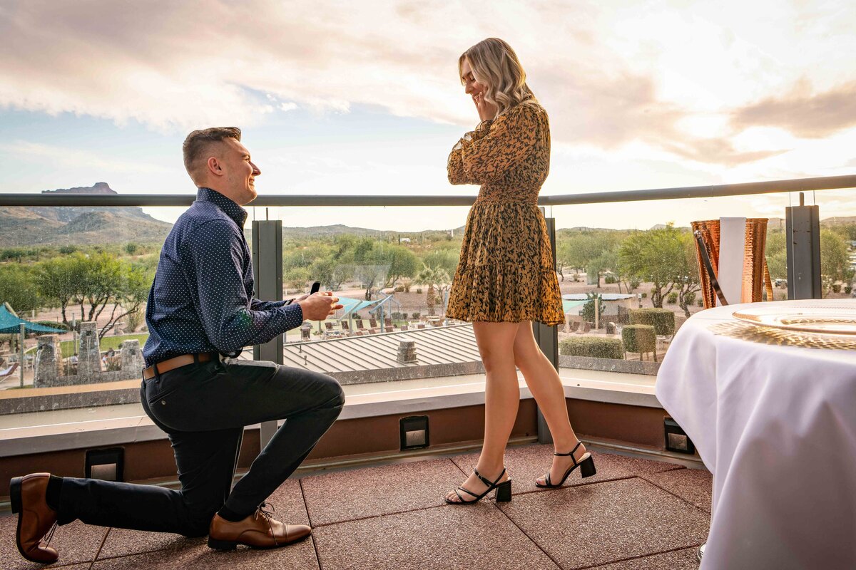 Man kneels to propose to his girlfriend on a balcony at sunset