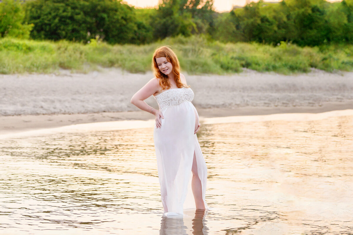 pregnant woman standing in the water on the beach for her summer maternity photography session in Burlington