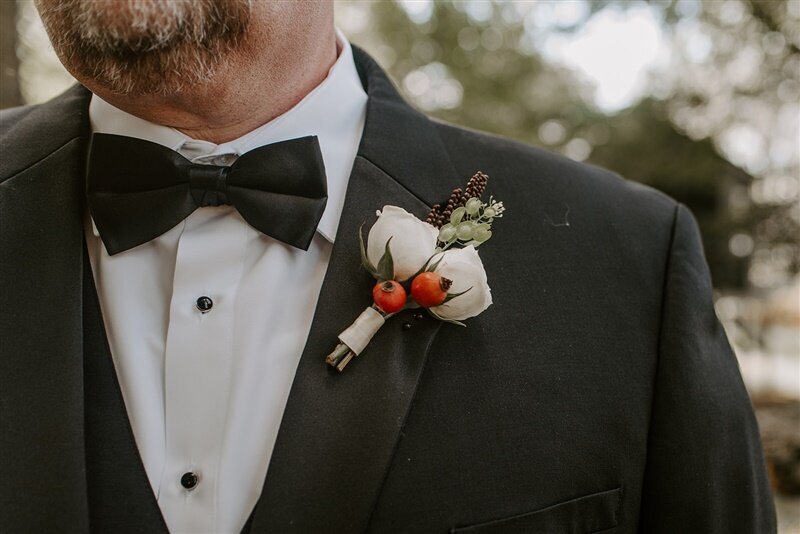 Father of the groom wearing a boutonniere  with orange rose hips, spray roses and seed pods