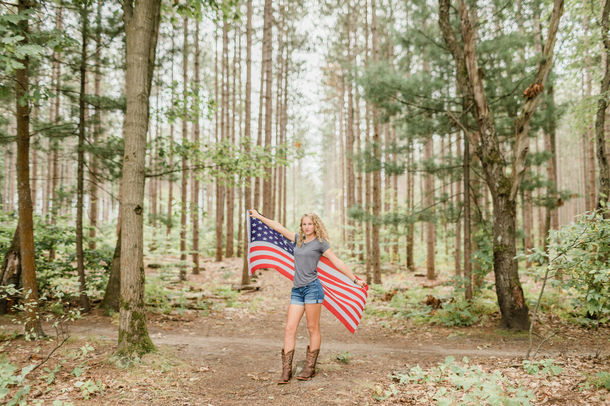 girl standing in the woods holding an american flag