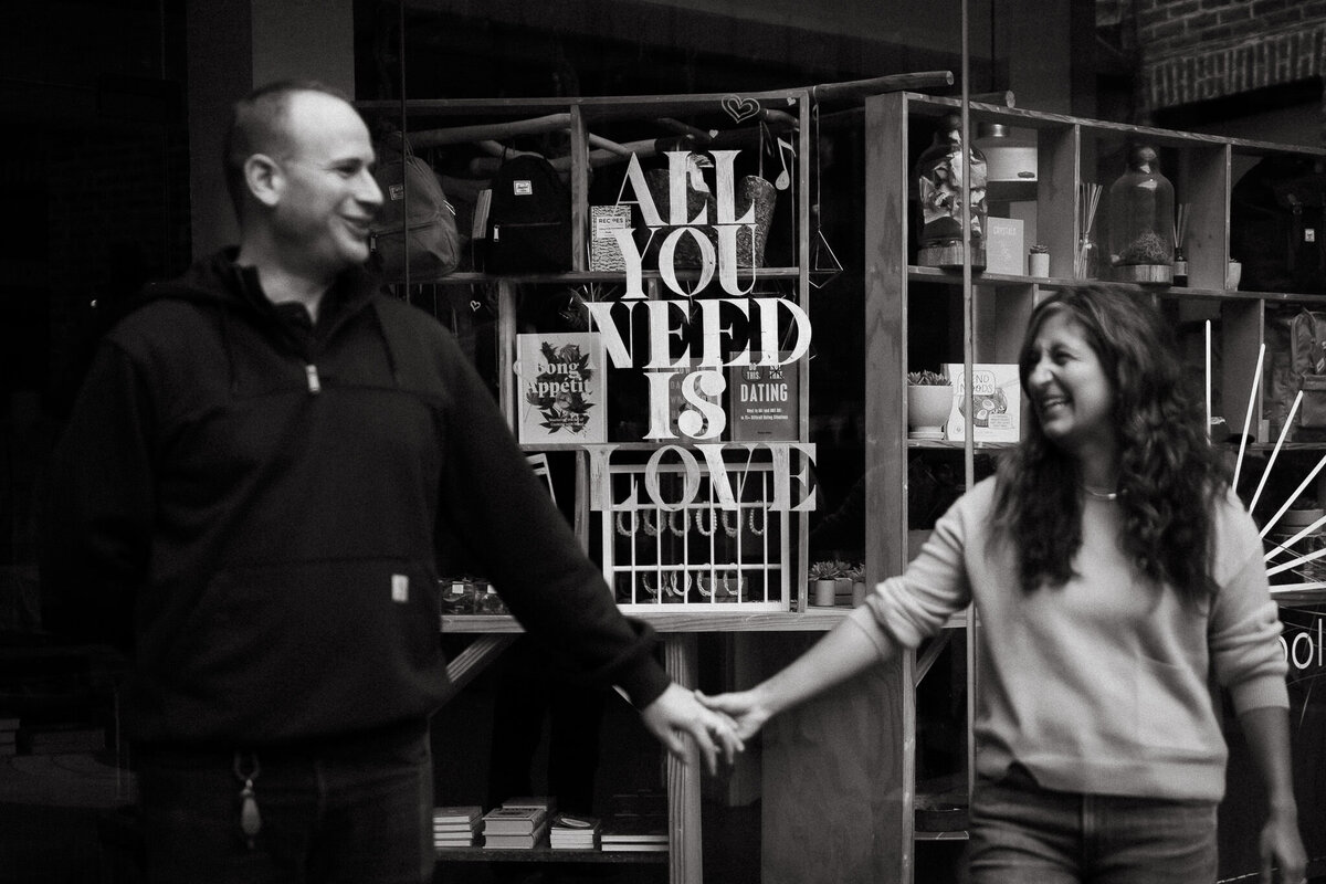 Black and white couples portrait. holding hands in Ghiradelli square in front of storefront that says All you need is love