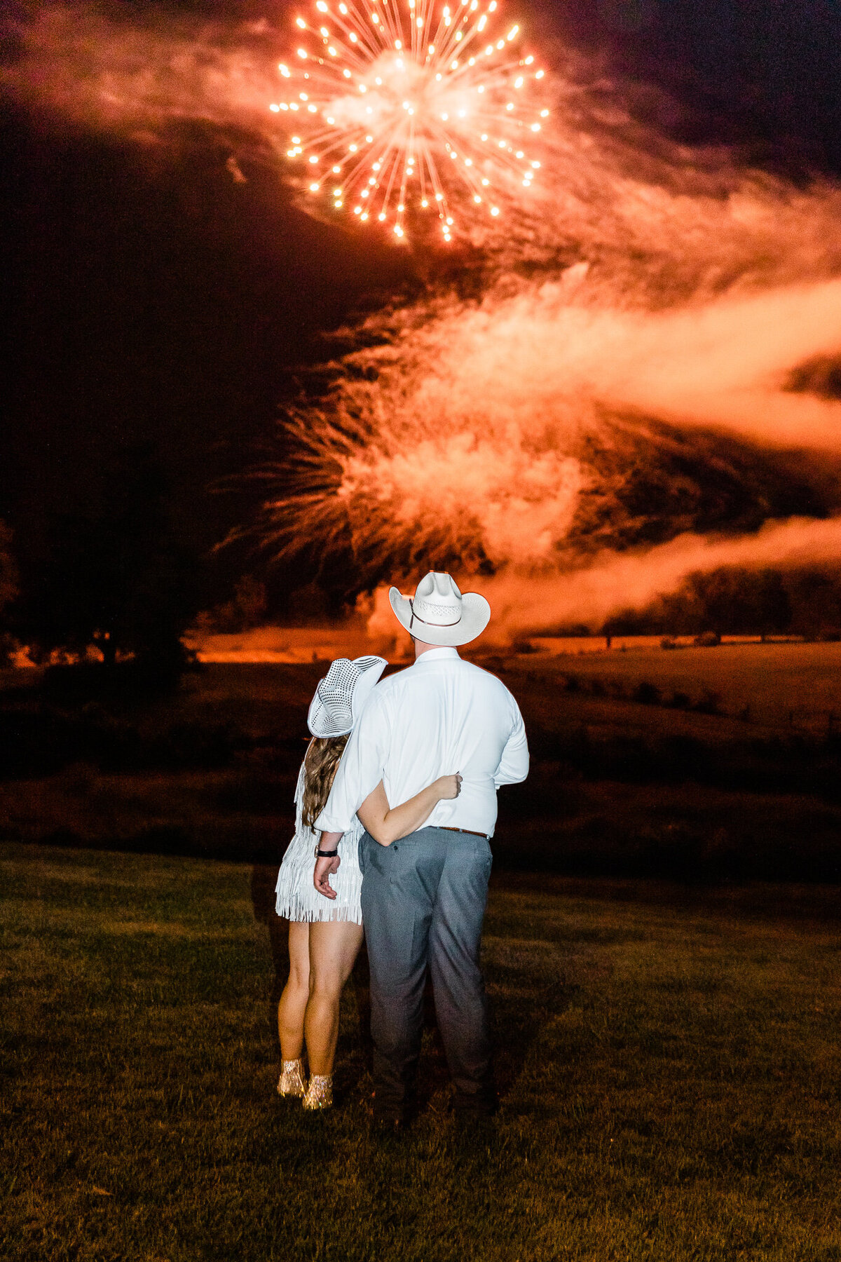 firework show at the end of a wedding reception with bride and groom holding each other as the red fireworks explode in the sky for an epic finale