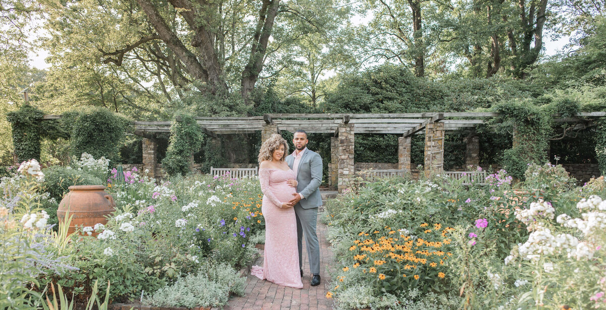 maternity photo in a garden, mom and dad standing betweens beautiful greenery scenery