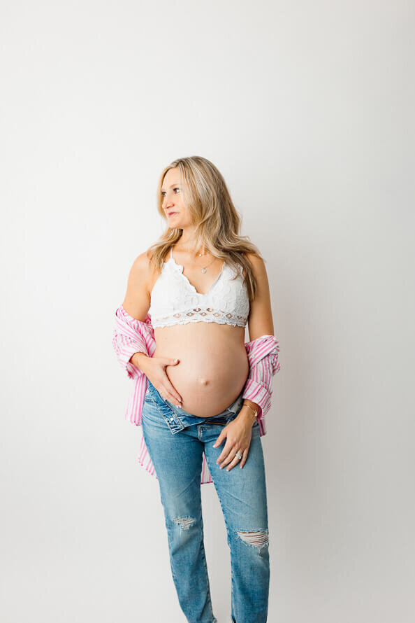 As a part of her maternity photos, a woman touches her belly and looks off to the side.