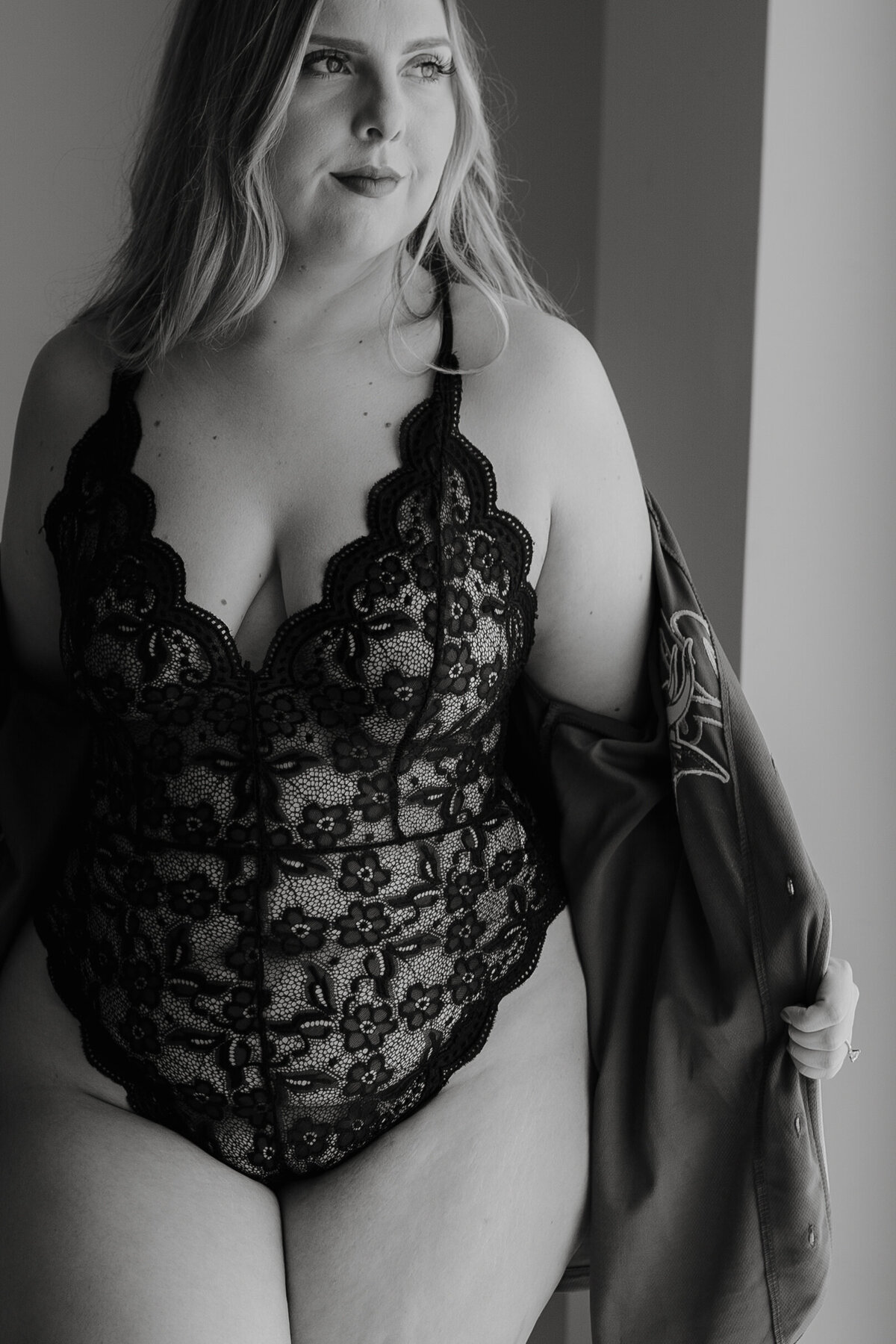 Black and white photo of woman in black lingerie with a robe on her arms looking off to the side