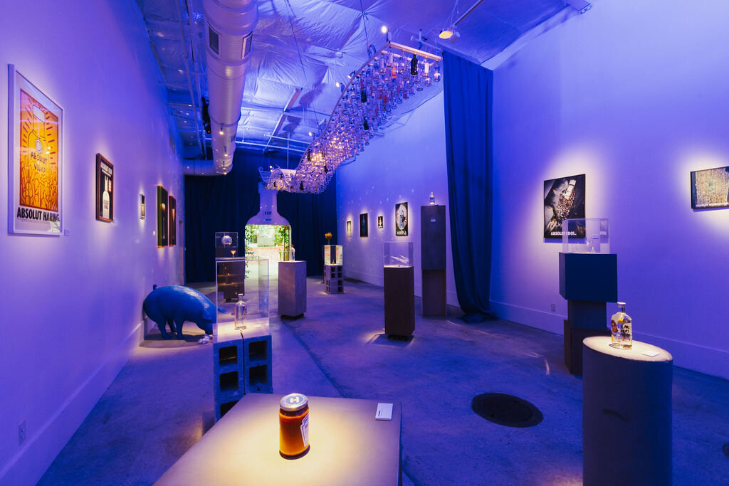 Dimly lit installation gallery space with art objects displayed on pedestals and dramatic lighting.