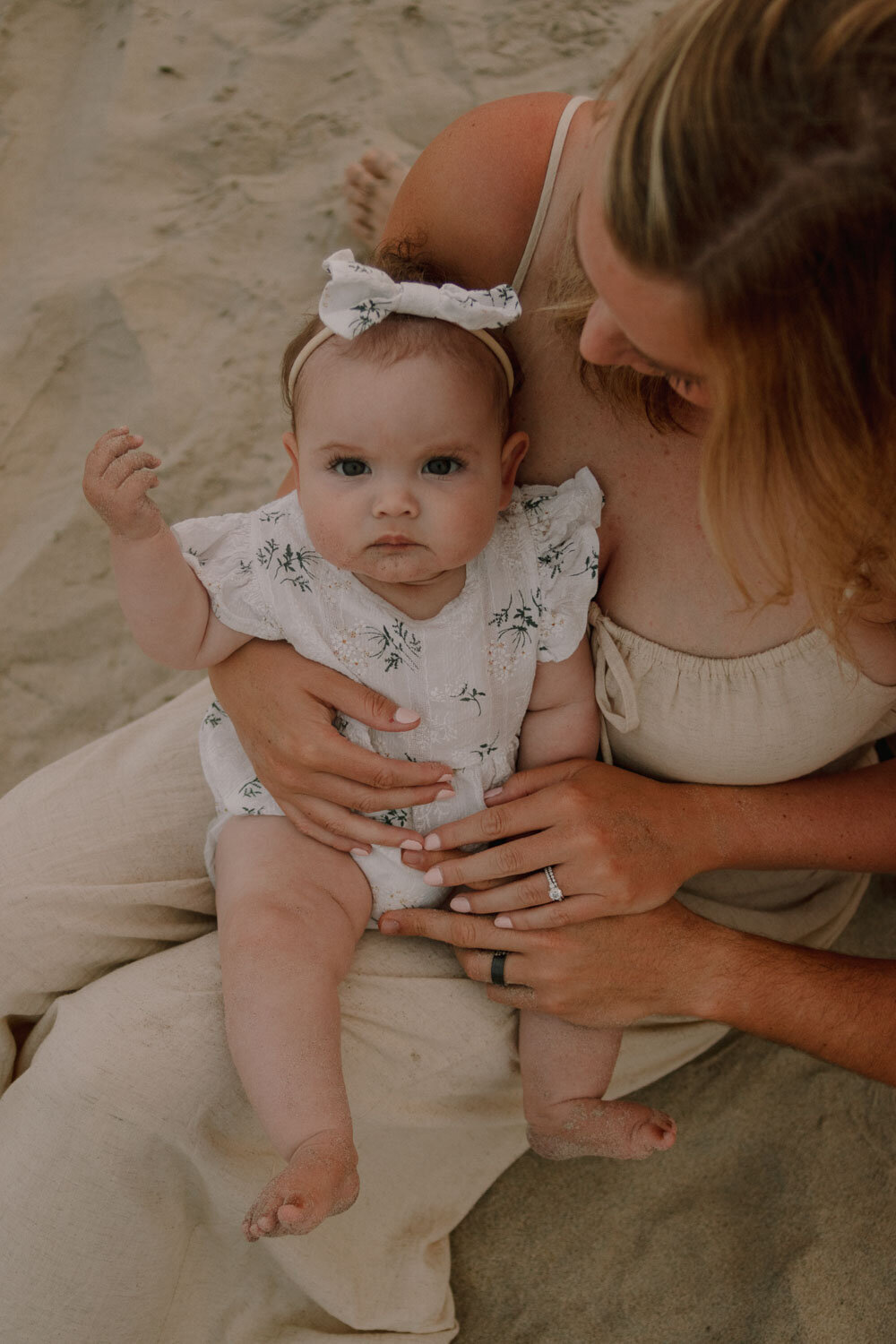 Baby sitting on parents’ lap on the sand, looking forward