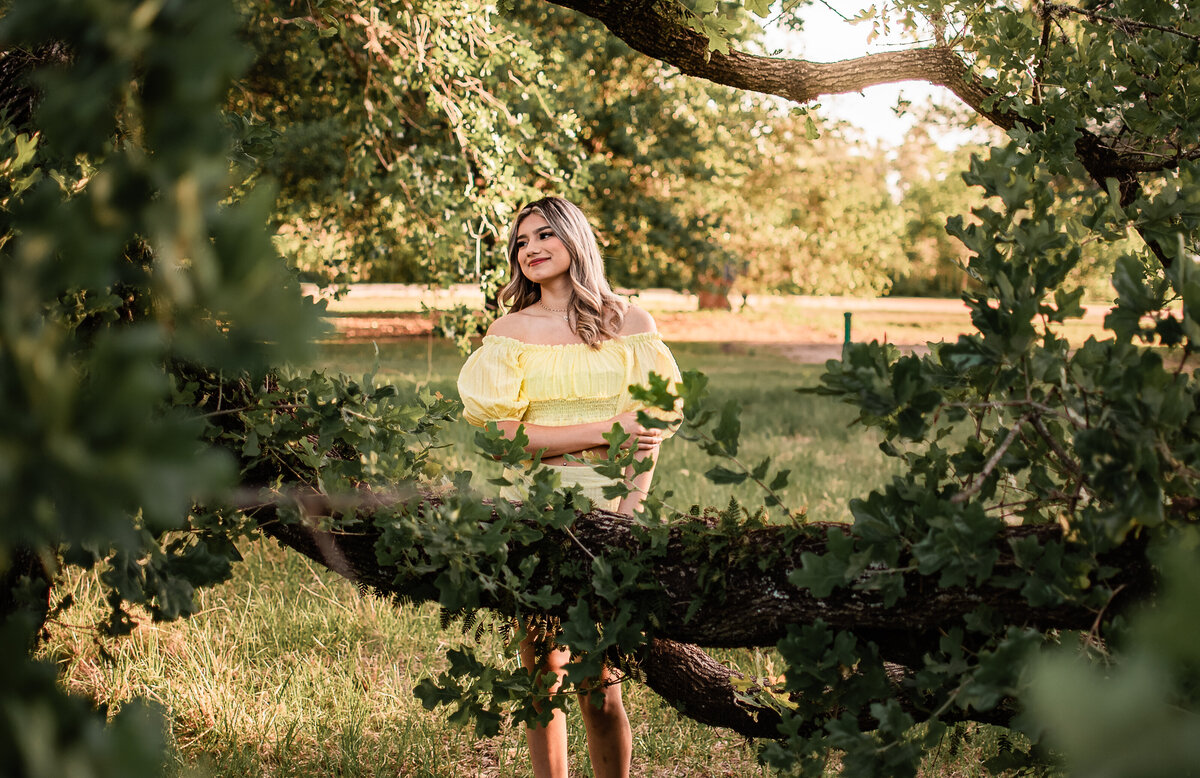 A Houston area senior stands behind an oak limb covered in vines and greenery.