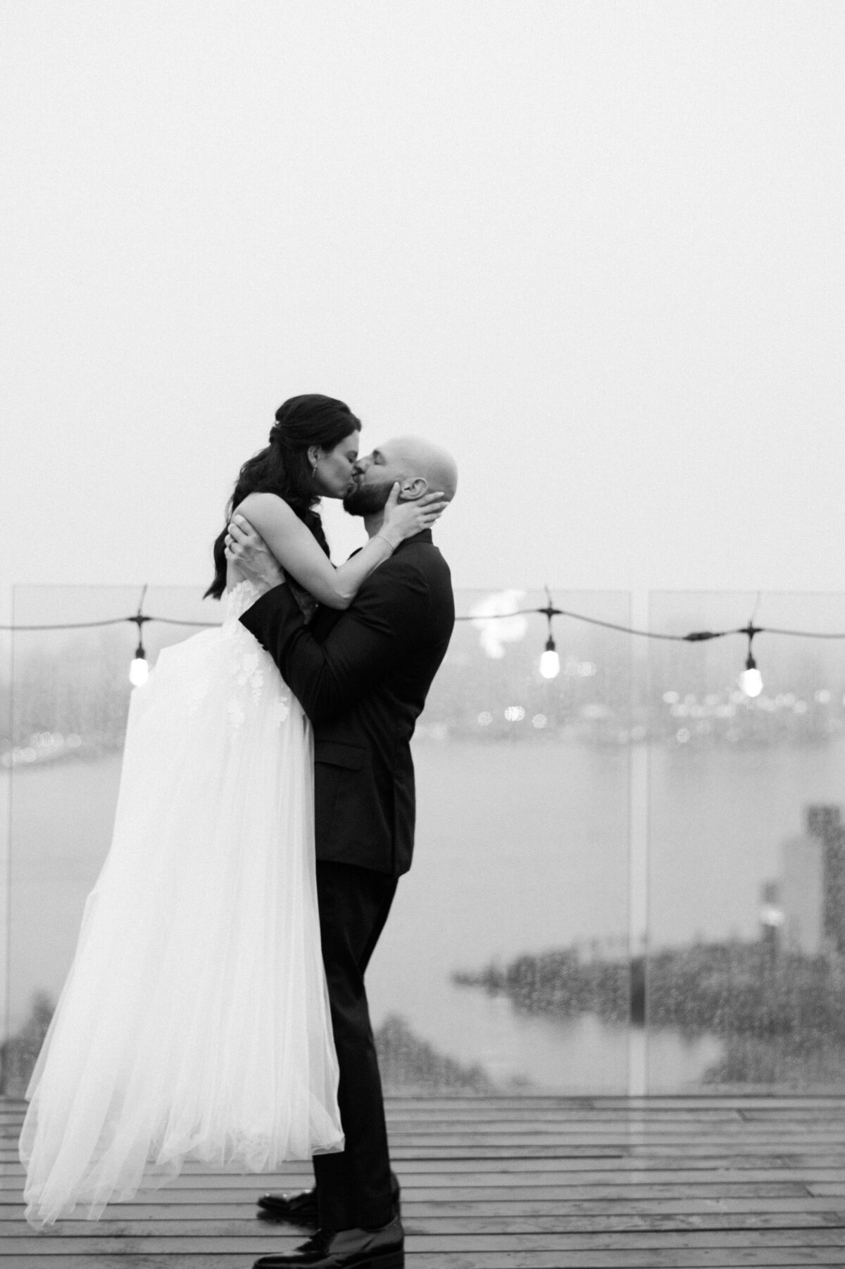 Groom holds his wife and kisses her in the rain 