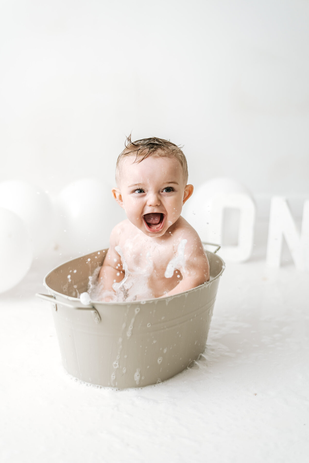 Baby boy splashing water in a bubble bath at a cake smash photoshoot in west sussex