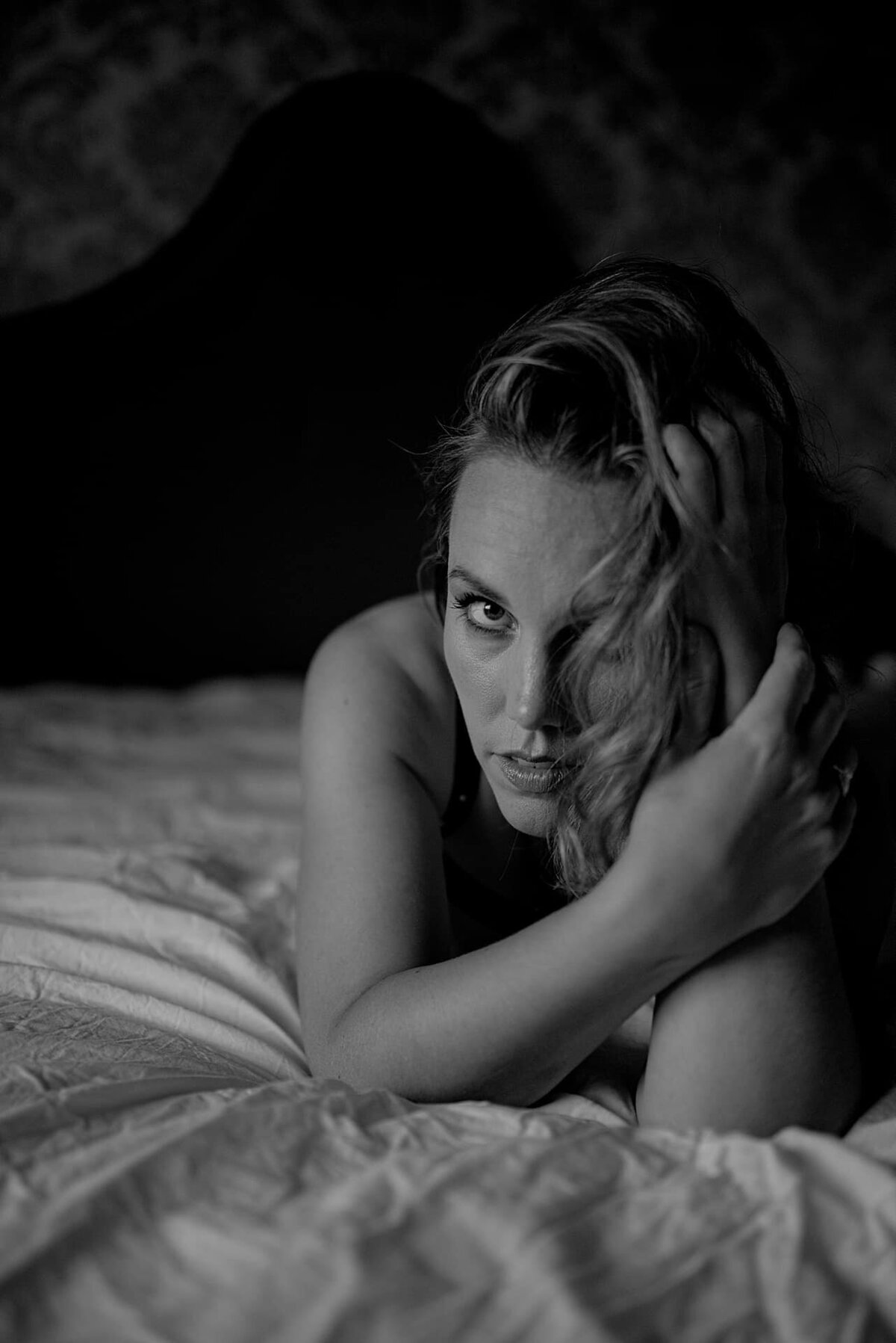 Under boudoirfotografering i Oslo ligger en kvinne på senga støtter hodet.