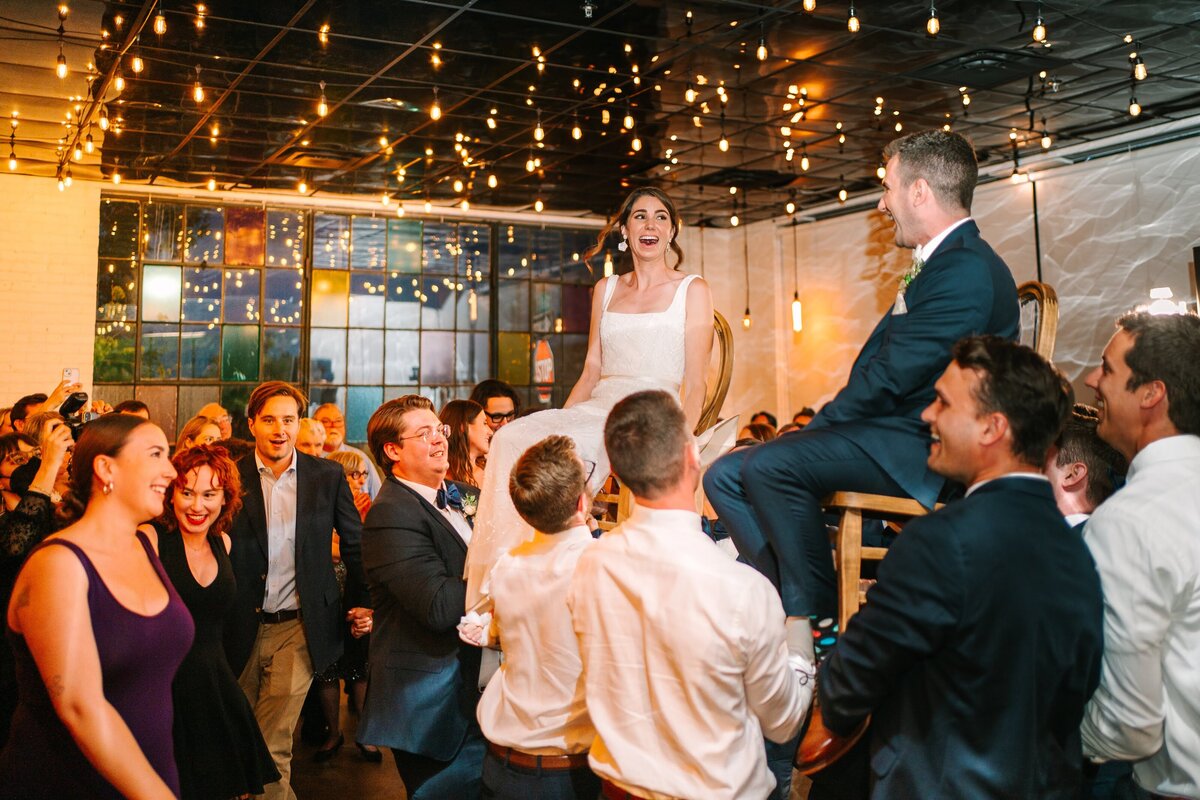 Bride and groom on chairs during their Hora dance at their reception.