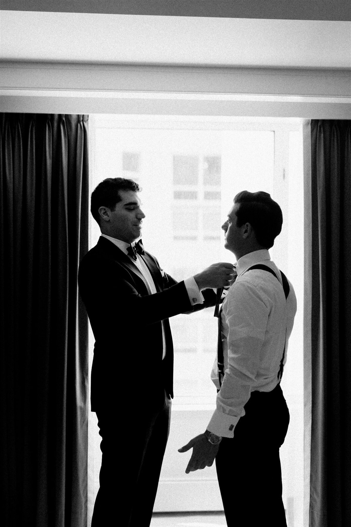 A picture of the groom getting help putting on his tie. 