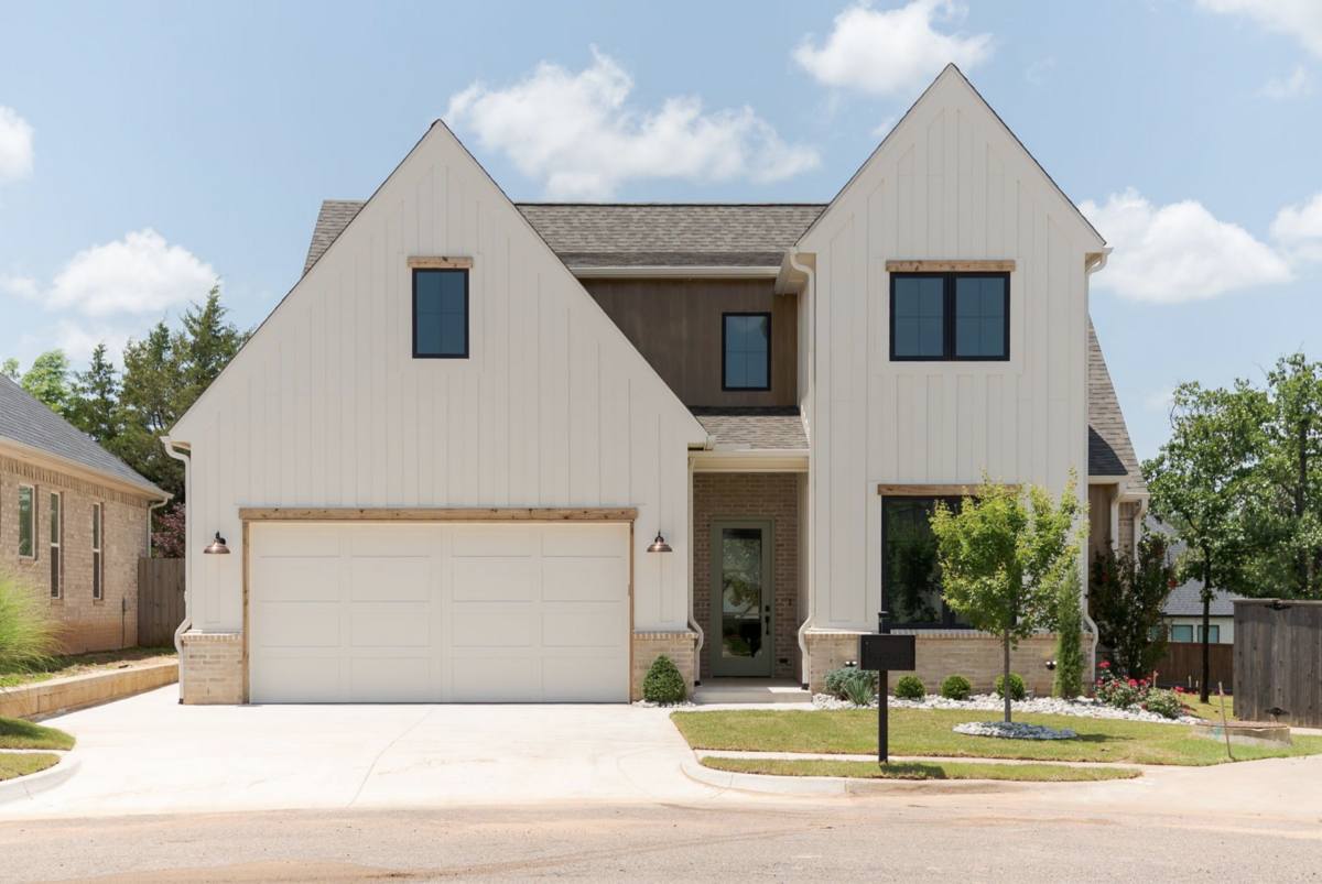 Modern farmhouse-style exterior with vertical white siding, warm wood accents, and contrasting black windows on a two-story home in Edmond, Oklahoma.