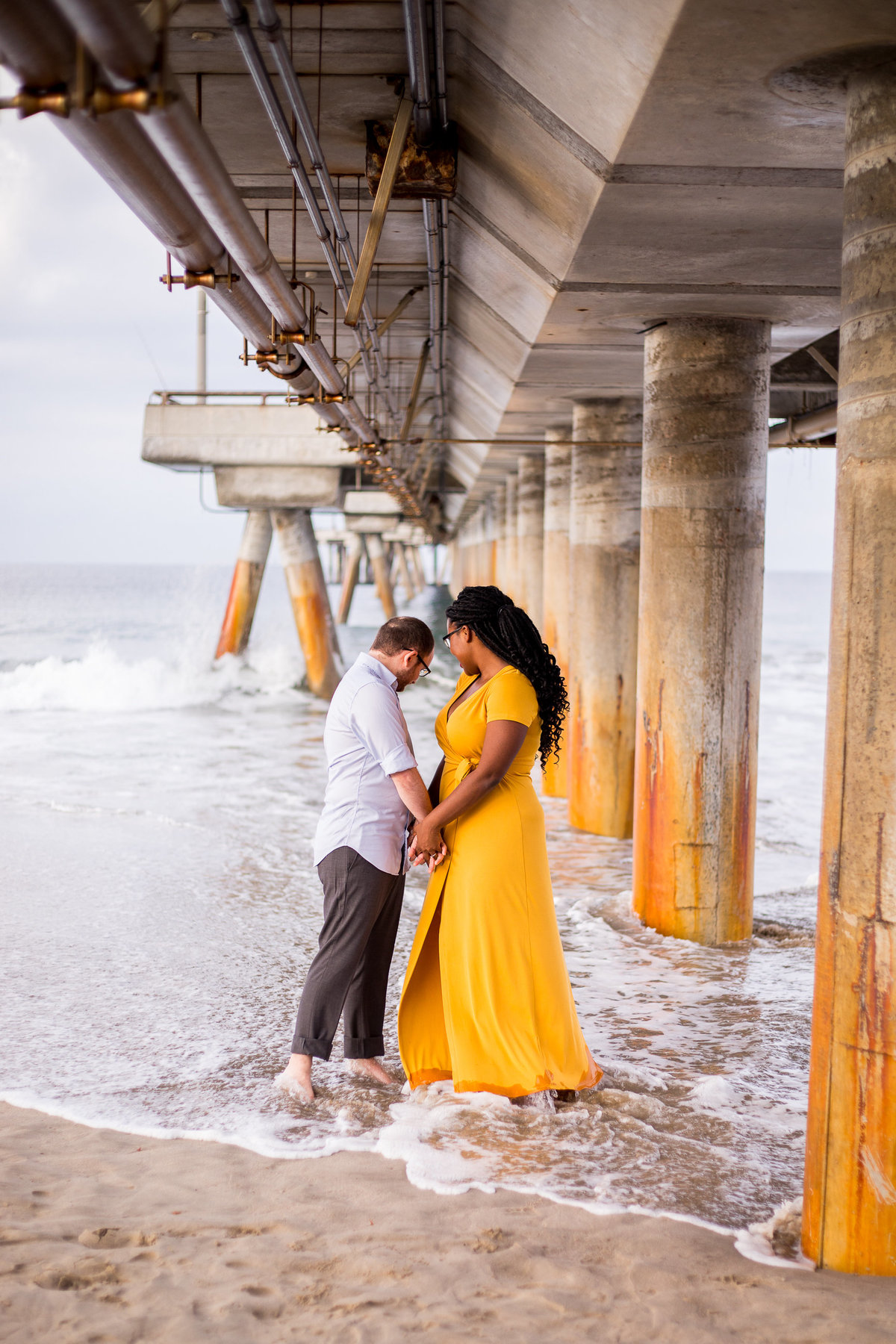 A couple holds hands in the shoreline under the Venice Beach Pier