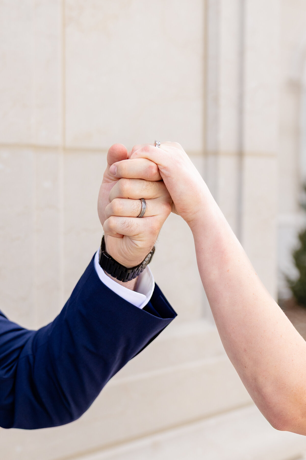 Bride and groom clasping hands, showcasing their wedding rings in front of the Taylorsville Utah Temple.