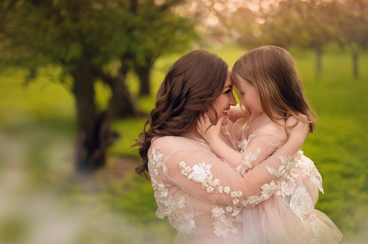 Mom and holds her young daughter standing in a Pewaukee orchard wearing matching floral gowns.